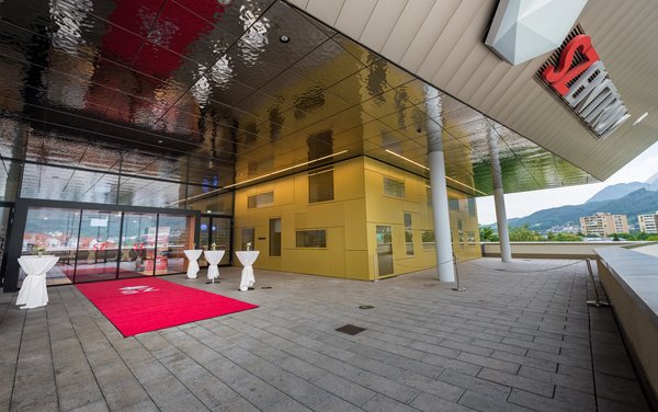 Eingang zum SZentrum mit rotem Teppich zur Glasschiebetür und mit Stehtischen.