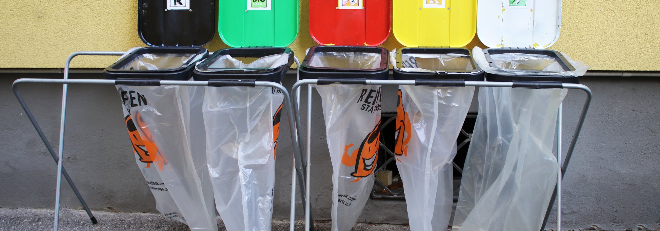 2 metallene Sackständer mit verschiedenfarbigen Deckeln für die 5 Fraktionen: Leichtverpackungen, Papier und Karton, Bio-Abfälle, Bunt- und Weißglas und Restabfälle. Inklusive transparente Abfallsäcke.