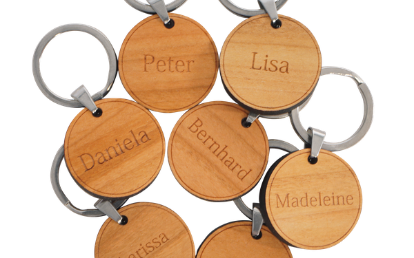 Sieben runde Holz-Schlüsselanhänger mit Metallring, graviert mit unterschiedlichen Vornamen.